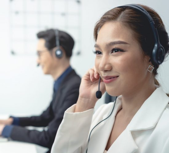 Asian call center agent team, customer service support wearing headset or headphone talking with customer in modern office.